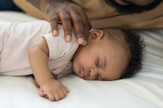 Close up of caring African American father hand gently touching and comforting newborn baby lying on white bed, tender family bonding and fatherhood moments at home