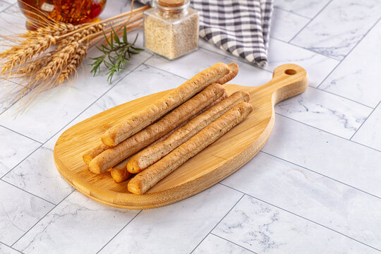 Crispy Italian grissini breadsticks with rosemary and wheat on wooden serving board appetizer