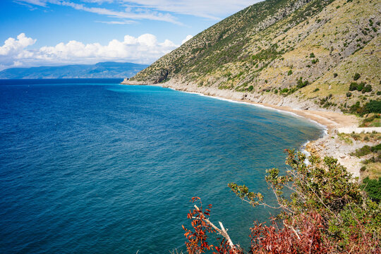 Curved bay with a narrow sandy beach below a green hillside and deep blue Mediterranean Sea, red foliage in the foreground near Kassab, Latakia, Syria