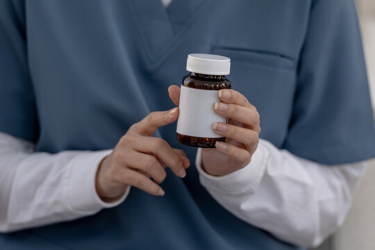 Professional nurse holding blank medicine bottle with focused care, showing medical prescription container in hospital clinic