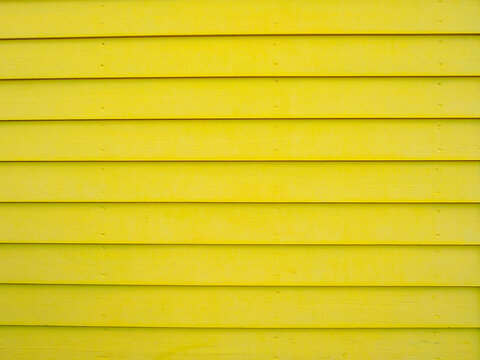 Fragment of bright yellow wooden facade surface - timber cladding - featuring horizontal lines. Slatted siding with a horizontal pattern of boards defined by gaps. Abstract textured surface for design