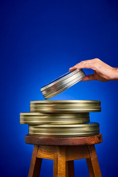 Close-up of a collection of analog film canisters on a wooden stool, against a blue background.