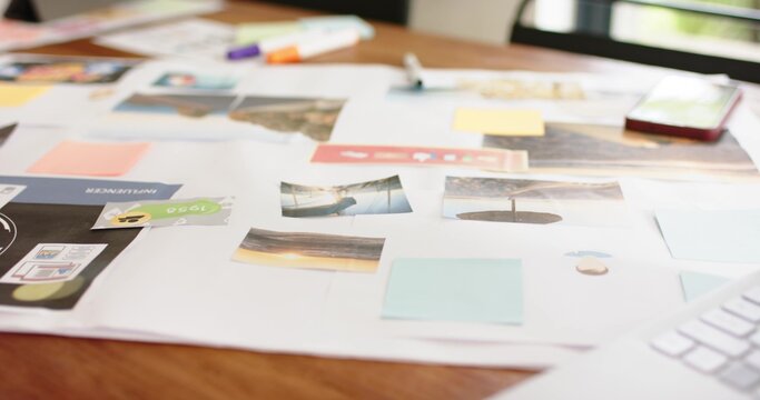 Large white sheet is lying on wooden table near window, holding prints and sticky notes