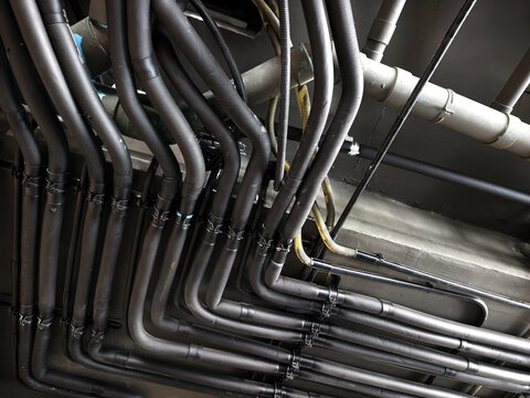 Organized electrical conduit and metal pipes with parallel right-angle bends along ceiling