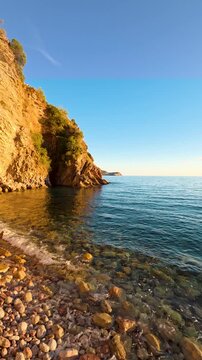 Scenic rocky beach with cliff and clear sea at sunset in Becici, Montenegro