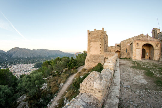 Mittelalterliche Burg mit Wehrturm und Steinmauern auf einem H&uuml;gel auf Mallorca, Berglandschaft im Hintergrund