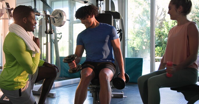 Young couple and friend exercising with dumbbells in gym, enjoying workout together