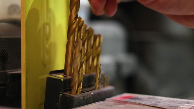 Close view of a worker's hand lifting a drill bit from a boxed assortment on a sturdy workshop bench, selecting an accessory for upcoming repair work. Slow motion 4K footage.