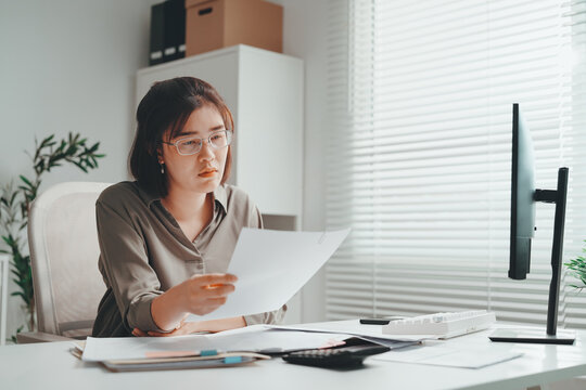 Business woman accountant reviewing financial documents at office desk, checking paperwork and reports with calculator and computer, focused on accounting, finance, audit and bookkeeping tasks.