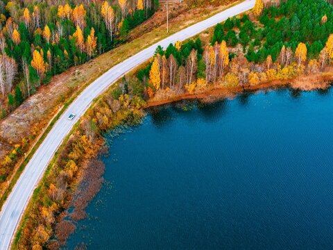 Aerial view of winding road beside a tranquil blue lake surrounded by vibrant autumn foliage