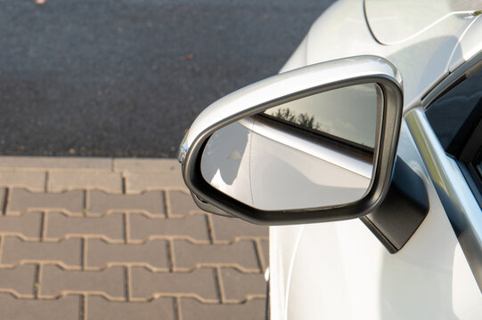 Side mirror of a white car parked beside a paved roadside in daylight