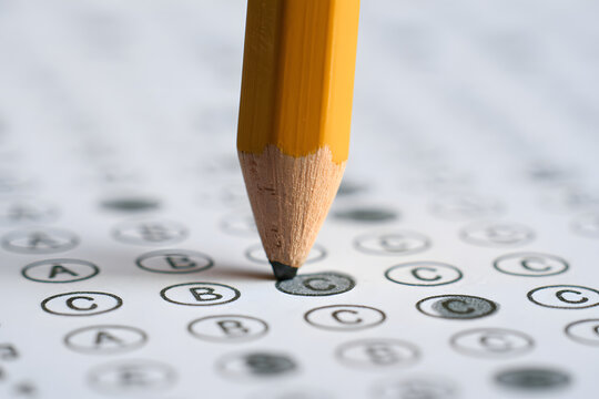 A detailed image of a yellow pencil placed over a bubble sheet for a multiple-choice test or survey, with the intent to mark an answer.