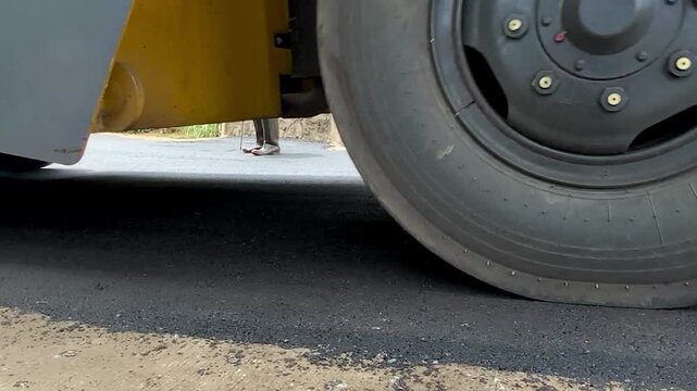 Close-up view of a heavy road roller machine wheel moving over freshly laid asphalt during road construction and paving work.