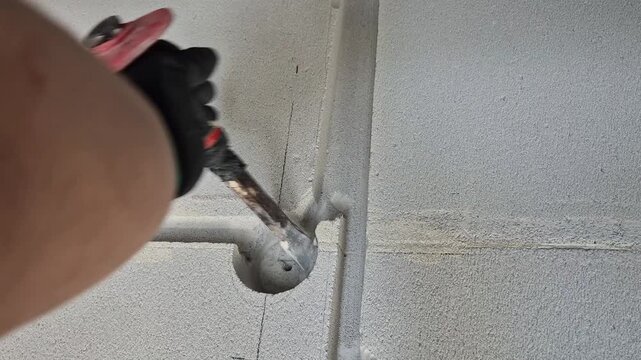 Close-up of a construction worker hands wearing protective gloves chiseling a groove in a gas concrete wall in slow motion.