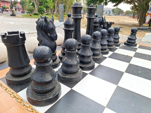 Large black chess pieces arranged on outdoor board for recreational activities.