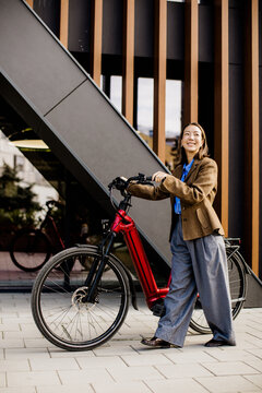 Woman stands beside electric bike near a modern building in daylight