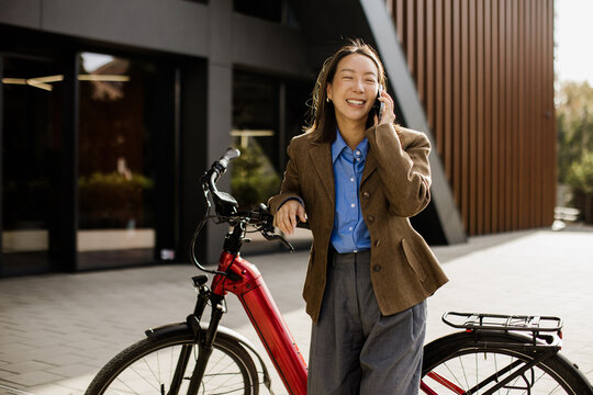 Young woman talking on phone while standing next to red bicycle in urban area