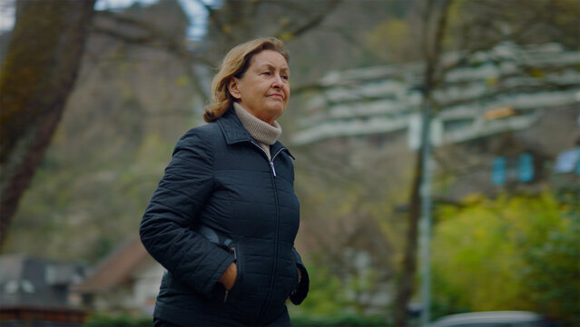 Senior Caucasian woman walking past trees and across a park lawn, independent lifestyle and daily exercise