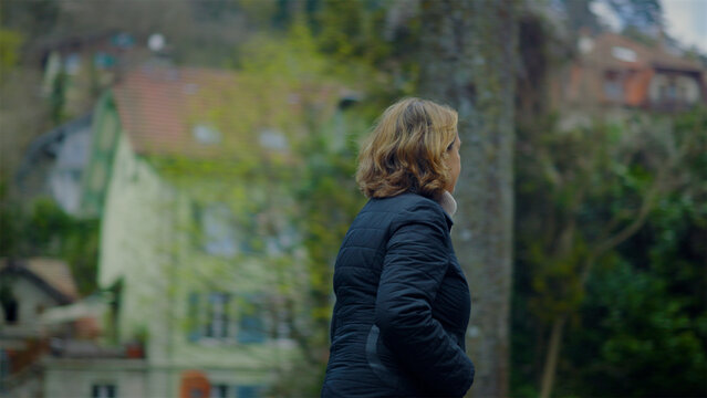 Senior Caucasian woman walking past trees and across a park lawn, independent lifestyle and daily exercise