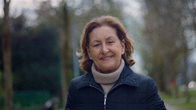 Smiling Caucasian older woman walking toward the camera in the park, happy and active senior lifestyle