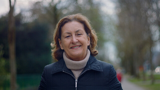 Smiling Caucasian older woman walking toward the camera in the park, happy and active senior lifestyle