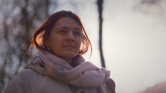 Young Caucasian woman standing in a sunlit winter park looking around, hope and fresh beginnings