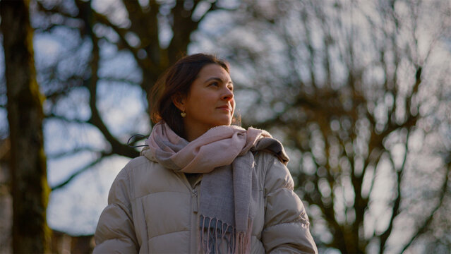 Young Caucasian woman standing in a sunlit winter park looking around, hope and fresh beginnings