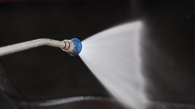 Car door is cleaned with a pressure washer at a self service car wash. Water spray removes dirt from the vehicle exterior surface. Washing process covers the side panel. 