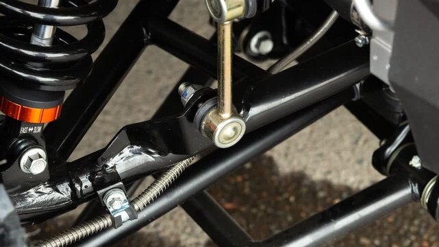 Detailed view of an all-terrain vehicle (ATV) suspension featuring coil spring, shock absorber, and metal linkages.