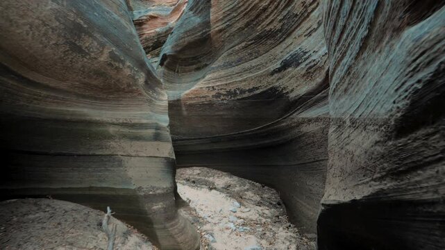 Camera moving forward through narrow deep sandstone slot canyon, showing smooth curved striped rock formations carved by water erosion on a dry rocky riverbed trail. Study of remote places in nature