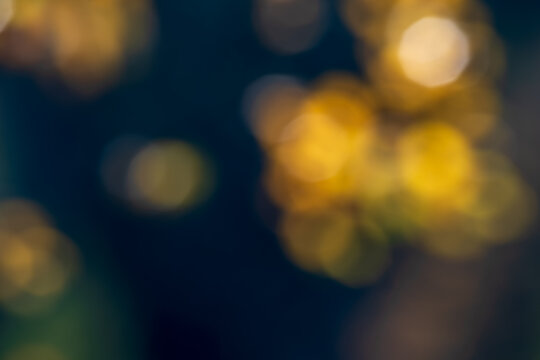 Abstract autumn background with blurred golden yellow birch leaves, warm amber bokeh lights and deep blue tones, creating a soft seasonal nature backdrop with copy space.