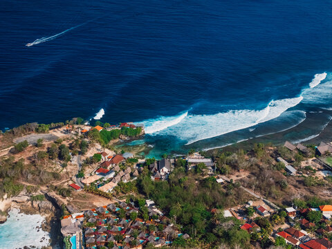 Ocean coastline with village and surfing waves on Nusa Ceningan, drone view