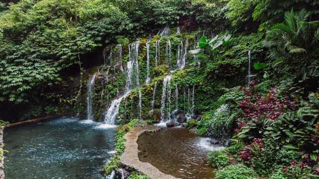 Waterfall cascading over mossy rocks surrounded by jungle foliage in Bali island