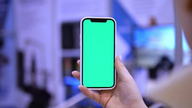 Hand holds smartphone with green screen. Background blurred, indoor setting. Phone steady, focused on screen