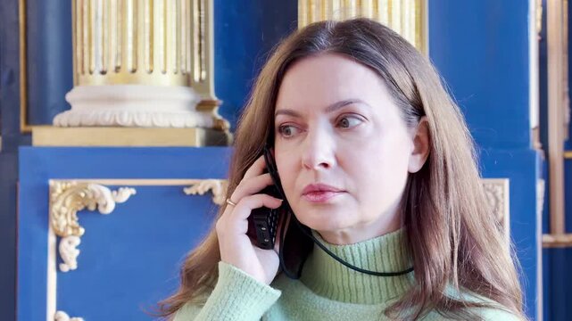 A curious woman listens to an audio guide inside the Catherine Palace, Pushkin, Russia. She feels fascinated by the majestic golden decor.