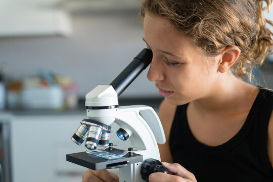 Student Examining Slide Through Microscope In Laboratory