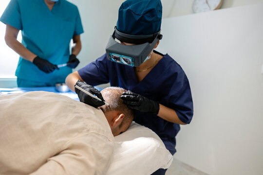 Specialist performing hair transplant procedure on male patient