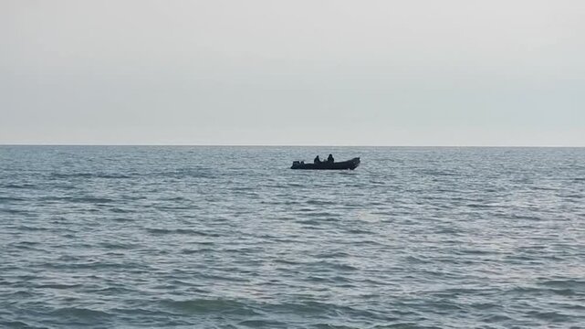 Rubber dinghy on waters of the Mediterranean Sea, with the silhouettes of people &ndash; dark evening view. Topics: sea ​​voyage, dangerous, sport, seascape