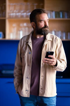 Bearded Man Using Smartphone in Modern Kitchen