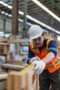 Plywood for woodworking is measured by a carpenter using a tape measure beside the wood workshop's nearby control panel.