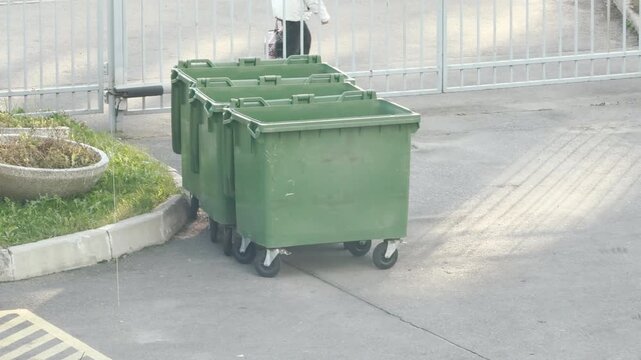 Green trash bins sit lined up near a fence in Pushkin, Russia. The still environment creates a calm and quiet mood during daily city routine.