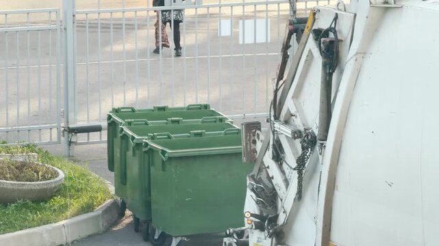 A garbage truck departs, leaving empty green bins along a fence in Pushkin, Russia. The scene brings a sense of relief, order, and calm satisfaction after a completed job.