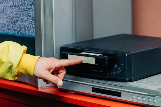 Hand in yellow sleeve inserting VHS tape into black vintage player.