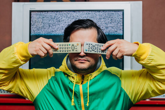 Man in yellow green tracksuit holding TV remote, static TV background