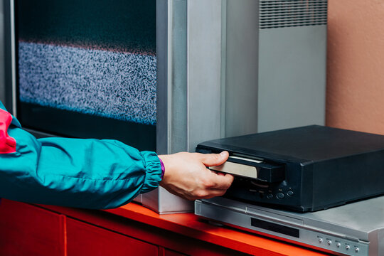 Hand in neon sleeve inserting VHS tape into vintage player