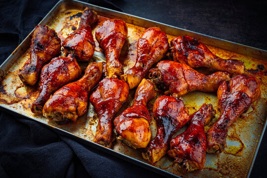Traditional oven roasted barbecue chicken drumsticks with hot honey chili sauce served as close-up in a skillet on rustic board