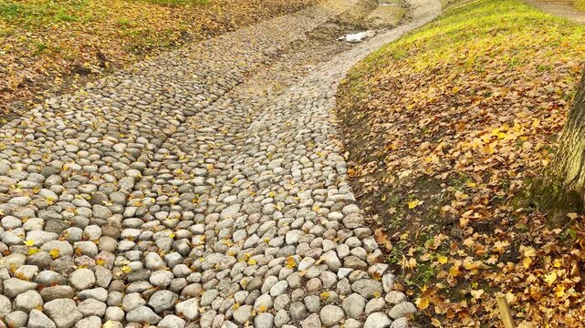 A stone cobblestone channel curves peacefully through fallen autumn leaves in Catherine Park, Pushkin, Russia. The slow motion view conveys a serene, tranquil mood in nature.