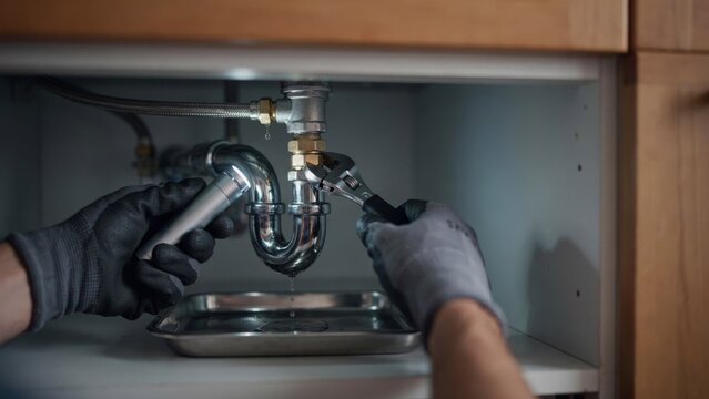 Plumber Repairing a Leaking Pipe Under a Sink to Prevent Water Waste and Household Damage
