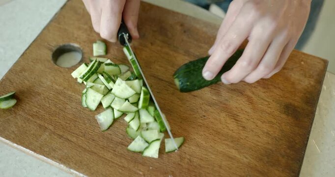 Close-up male hand cut cucumber with knife on wooden cutting board. 4K 10-bit