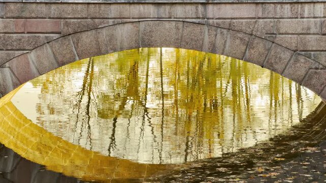 A stone arch frames vibrant golden reflections on calm water in Catherine Park, Pushkin, Russia. The glowing autumn light creates peaceful, dreamy, and nostalgic feelings.